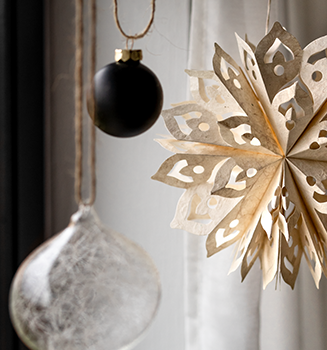 Papierstern vor einer dunklen und einer gläsernen Christbaumkugel