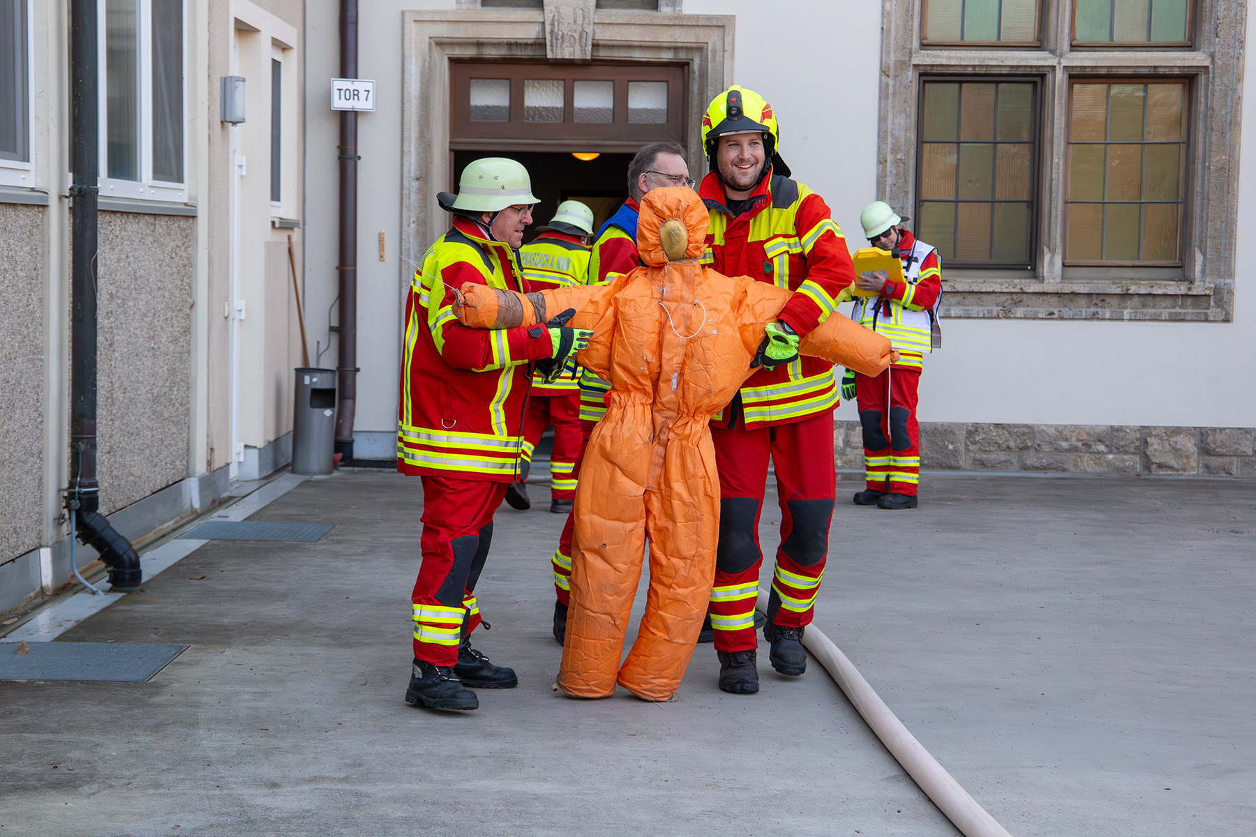 Zwei Feuerwehrmänner tragen orange Puppe