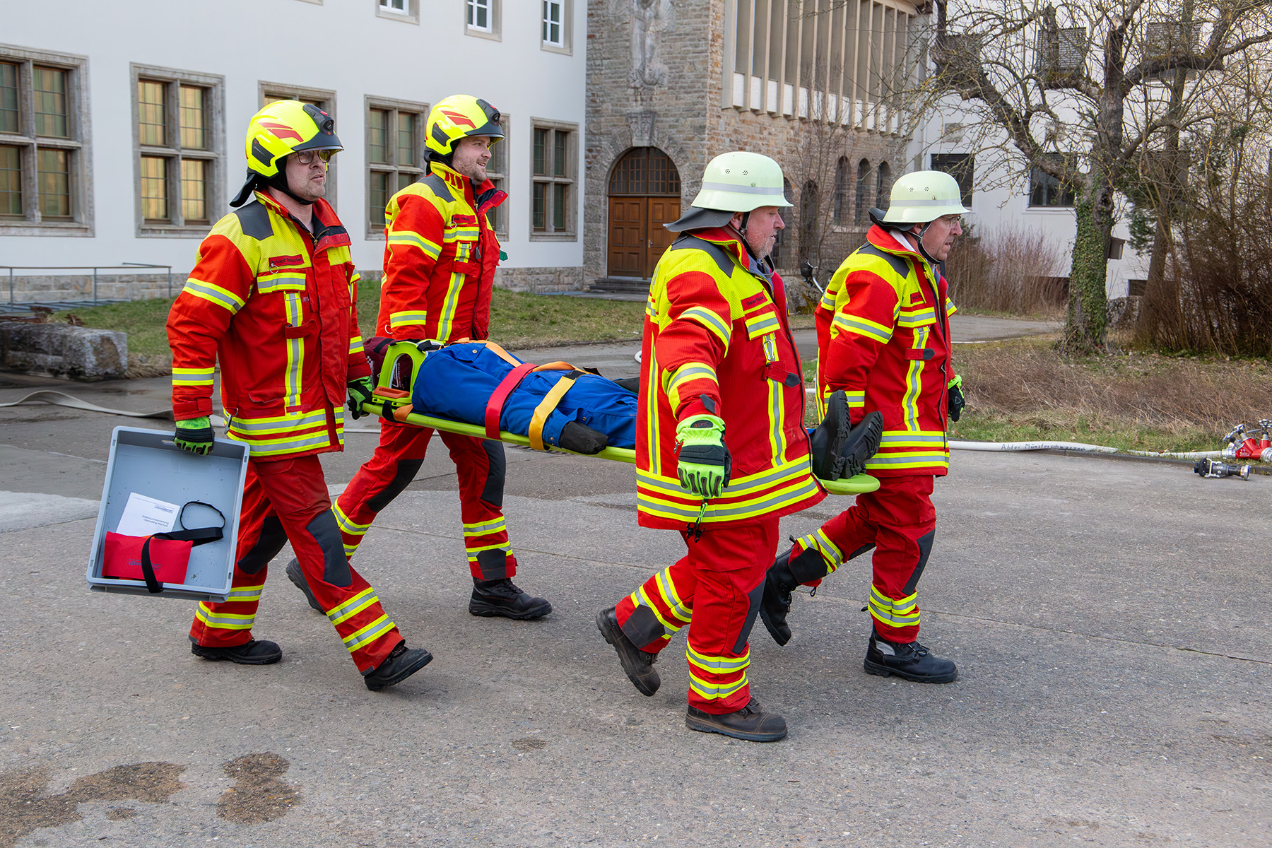 Vier Feuerwehrmänner tragen Puppe auf einer Trage