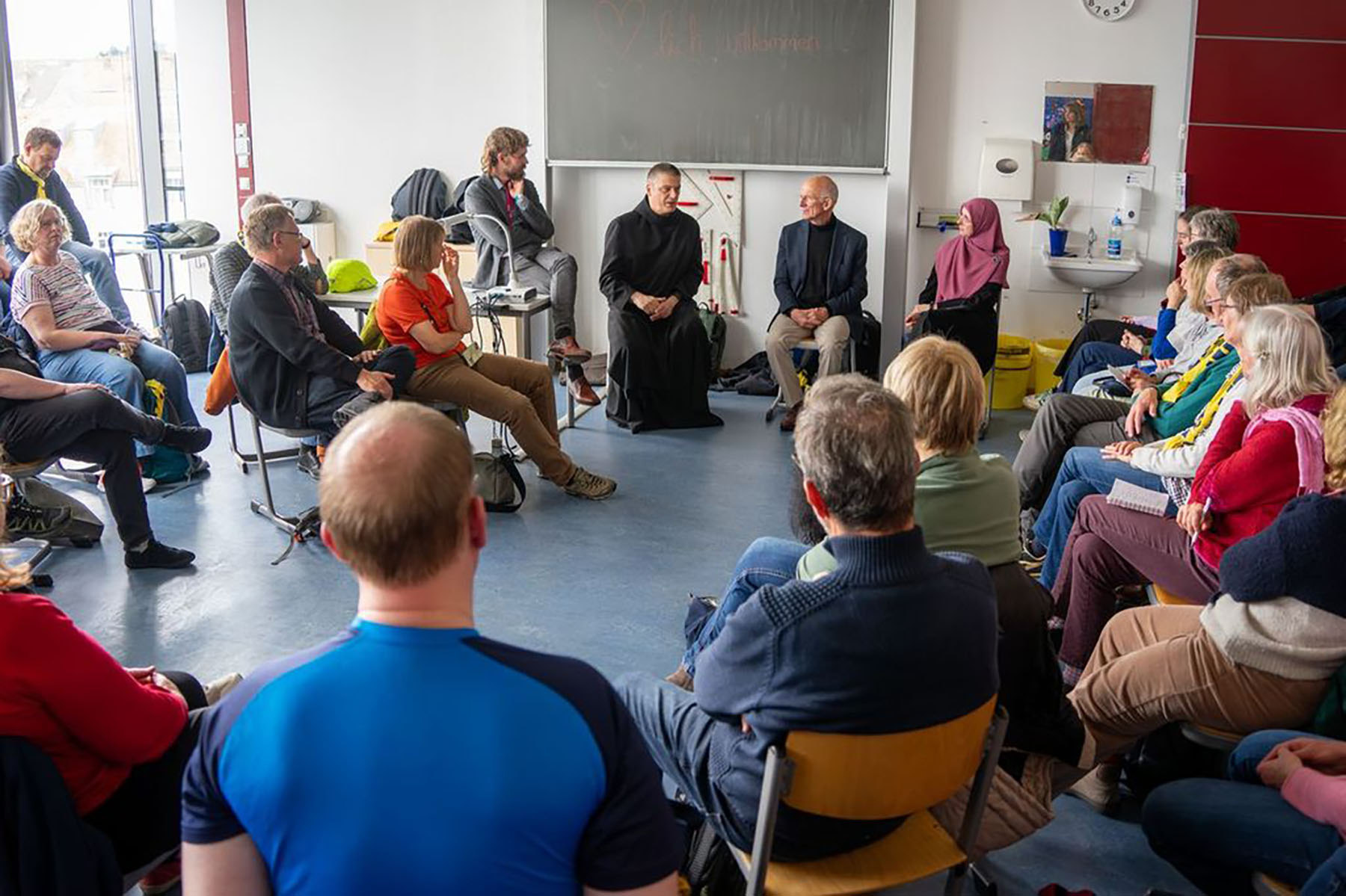 Größere Gruppe sitzt in einem Klassenzimmer