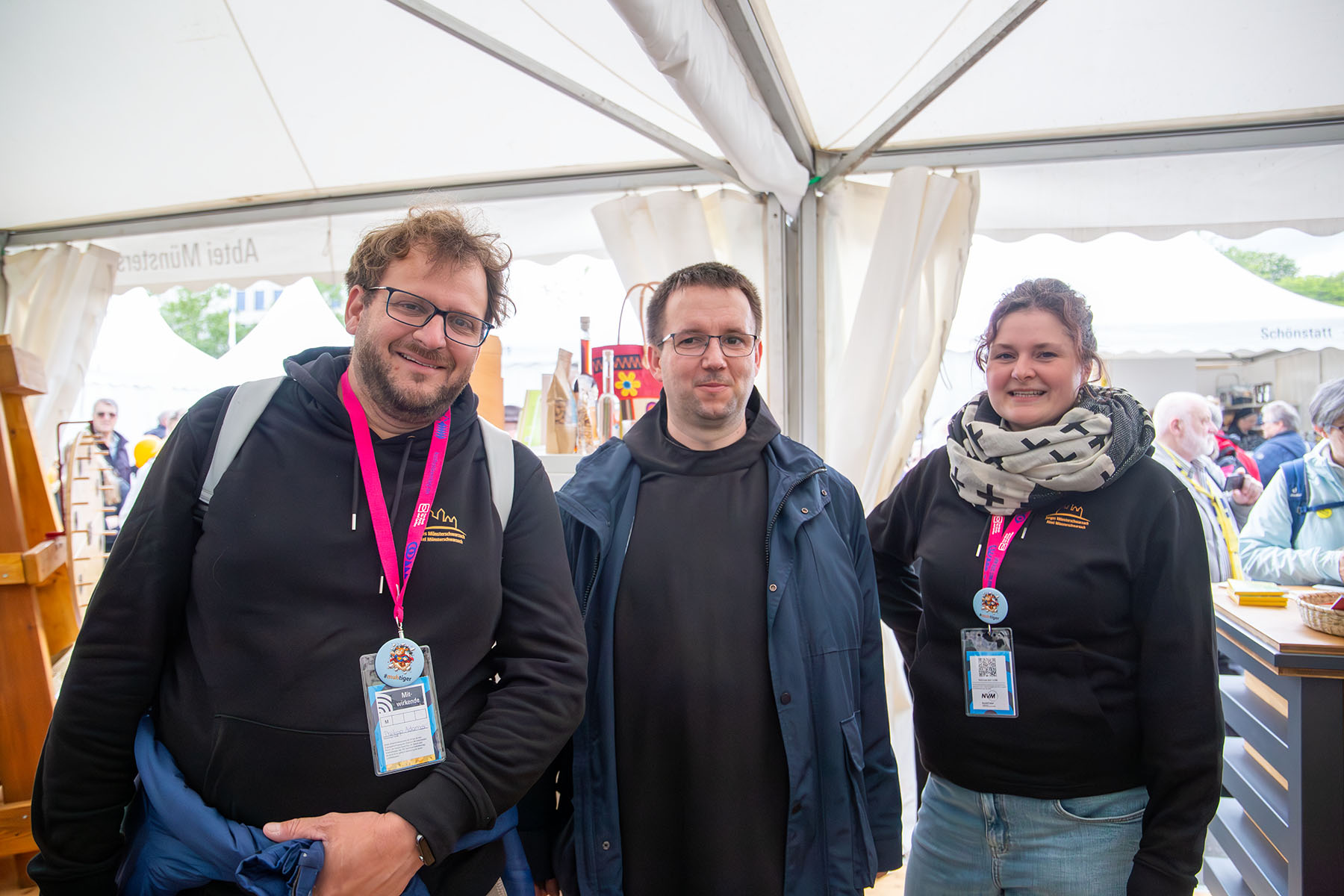 Junger Mann, Mönch und junge Frau am Messestand