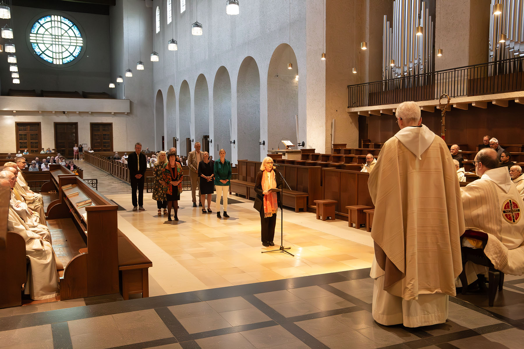 Sieben Menschen im Altarraum, eine Frau steht am Mikrofon, vorne sind zwei Priester