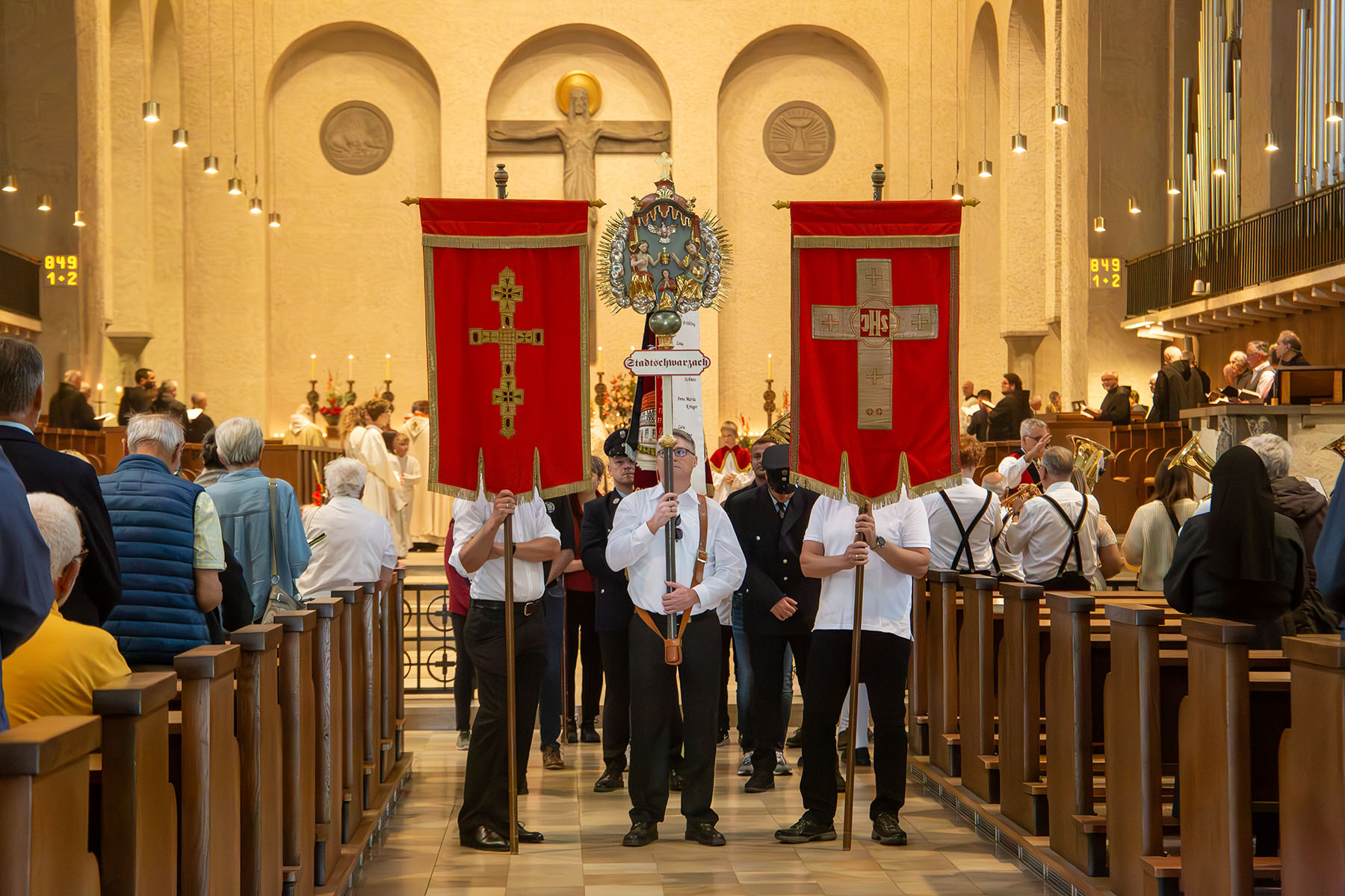 Drei Männer mit zwei Fahnen und einem Silberkreuz im Mittelgang der Kirche