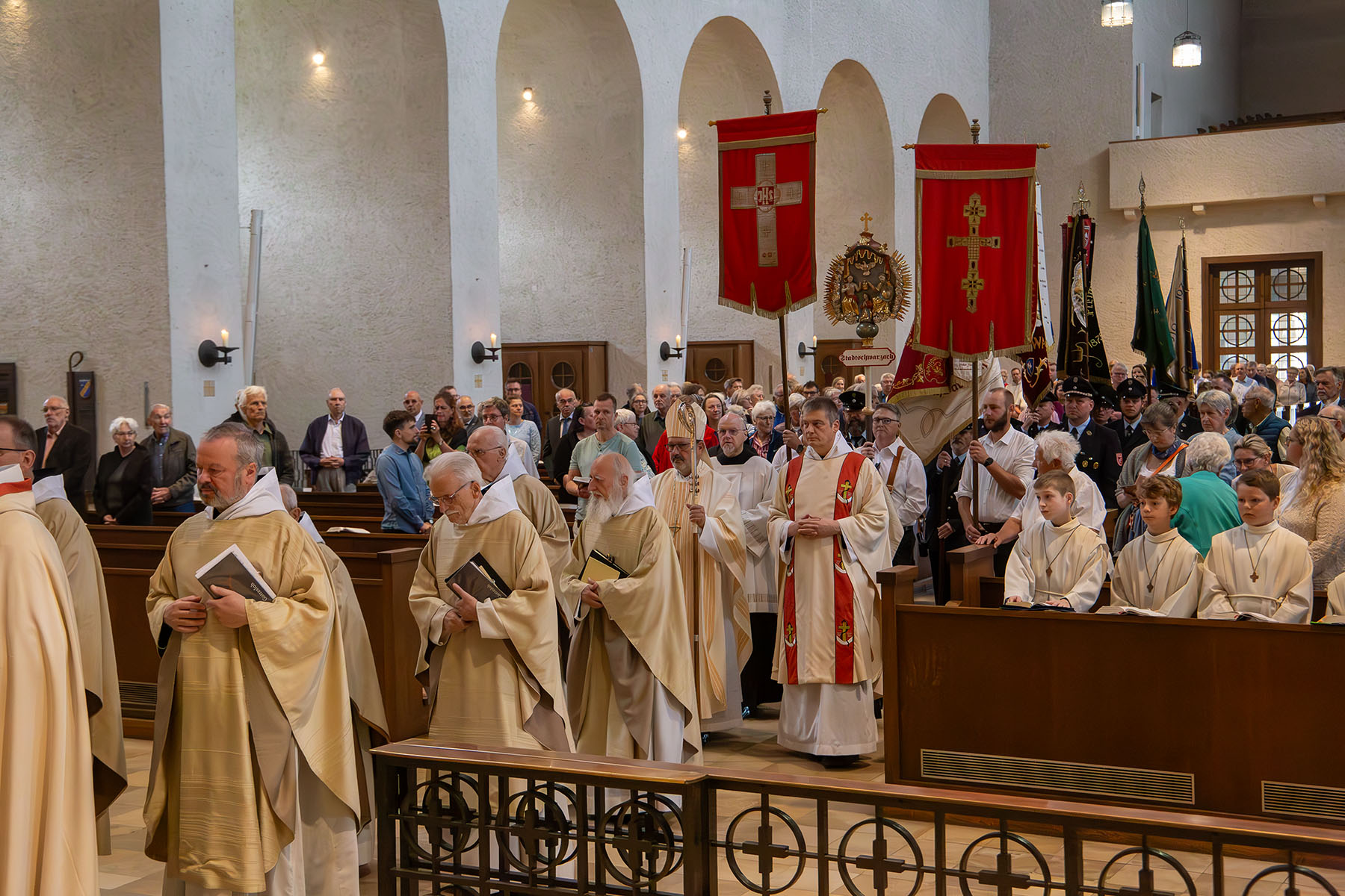 Gruppe von Priestern zieht in Kirche ein, im Hintergrund viele Fahnen