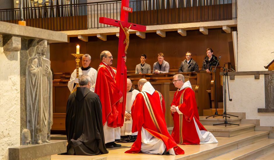 Mönche knien vor rotem Kreuz